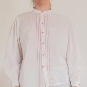 Blusa camponesa vintage branca com estampa floral, manga comprida, fechamento frontal com botões, ombros franzidos e gola mandarim.