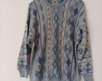 May include: A gray, blue, and beige patterned sweater with a crew neck and long sleeves. The sweater features a diamond and geometric design. The garment is displayed on a wooden hanger against a white background.