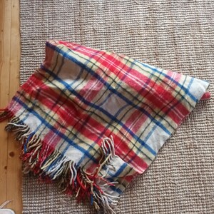 May include: A folded plaid blanket with red, white, blue, and yellow stripes. The blanket has a fringed edge with red, yellow, and blue tassels. The blanket is made of a soft, woven material.