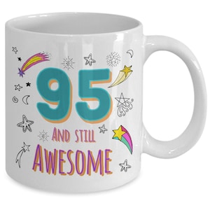 May include: White ceramic coffee mug with a teal number 95 and the text "and still awesome" in purple. The mug is decorated with colorful stars and shooting stars.