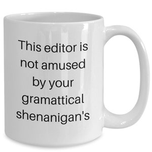 Może przedstawiać: Biały ceramiczny kubek do kawy z czarnym tekstem, kt&oacute;ry brzmi "This editor is not amused by your grammatical shenanigans".
