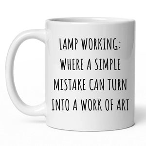 May include: White ceramic coffee mug with the text "LAMP WORKING: WHERE A SIMPLE MISTAKE CAN TURN INTO A WORK OF ART" in black. The mug has a curved handle and a cylindrical shape.