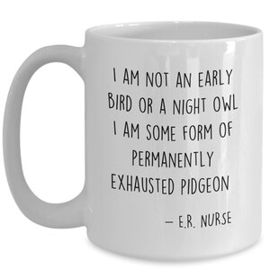 May include: White ceramic coffee mug with black text that reads: "I am not an early bird or a night owl. I am some form of permanently exhausted pigeon - E.R. Nurse"
