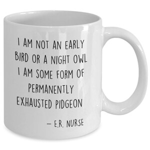 May include: White ceramic coffee mug with black text that reads "I am not an early bird or a night owl. I am some form of permanently exhausted pigeon - E.R. Nurse."