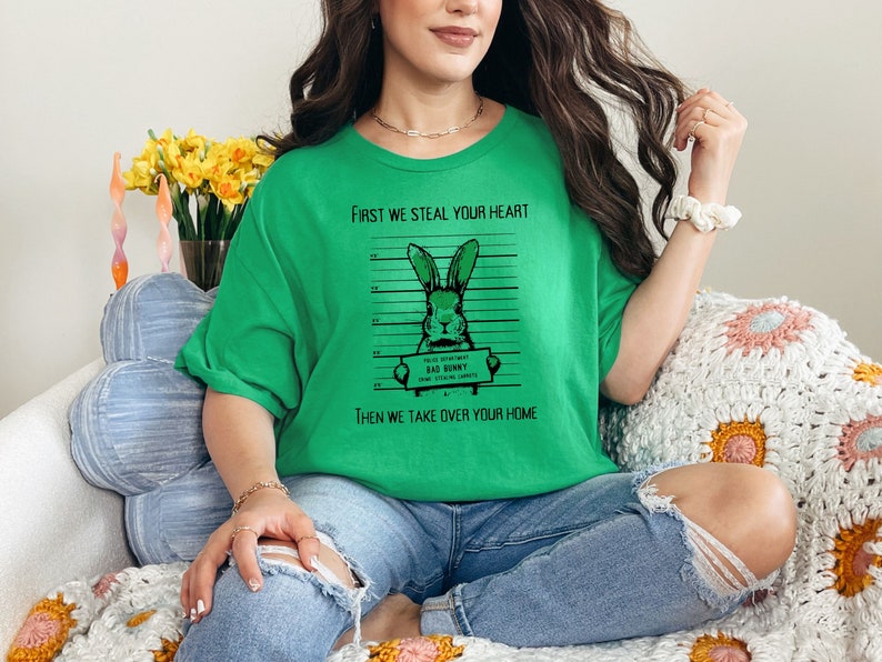 K&ouml;nnte beinhalten: Gr&uuml;nes T-Shirt mit einem Grafikdruck eines Kaninchens in einer Polizeiaufstellung. Der Text auf dem Shirt lautet "First we steal your heart, then we take over your home".