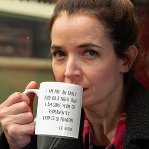 May include: White ceramic mug with black text that reads "I am not an early bird or a night owl. I am some form of permanently exhausted pigeon - E.R. Nurse".