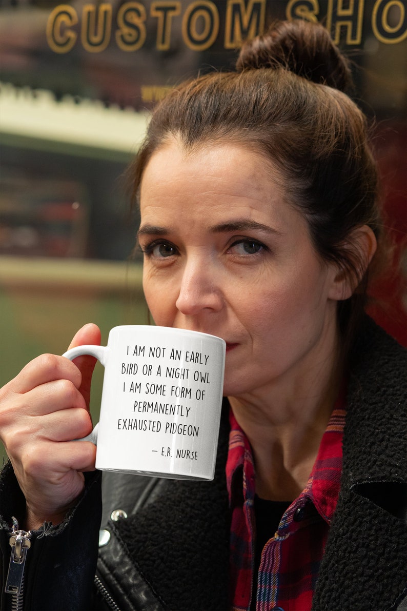 May include: White ceramic mug with black text that reads "I am not an early bird or a night owl. I am some form of permanently exhausted pigeon - E.R. Nurse".