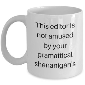 Może przedstawiać: Biały ceramiczny kubek do kawy z czarnym tekstem, kt&oacute;ry brzmi "This editor is not amused by your grammatical shenanigans".