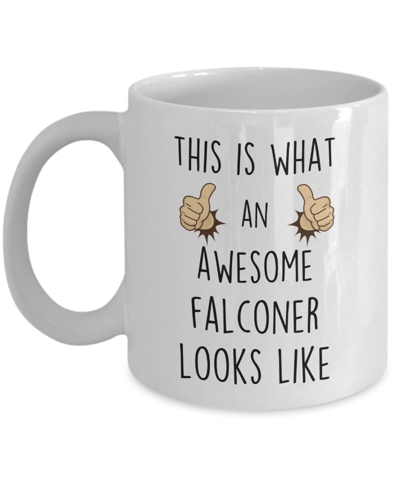 May include: White ceramic coffee mug with a black graphic that says "This is what an awesome falconer looks like" with two thumbs up emojis on either side of the text.