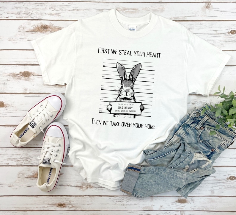 K&ouml;nnte beinhalten: Wei&szlig;es T-Shirt mit einer Schwarzwei&szlig;illustration eines Kaninchens mit dem Text "First we steal your heart" und "Then we take over your home". Das Kaninchen h&auml;lt ein Schild mit der Aufschrift "Police Department Bad Bunny Crime: Stealing Carrots".