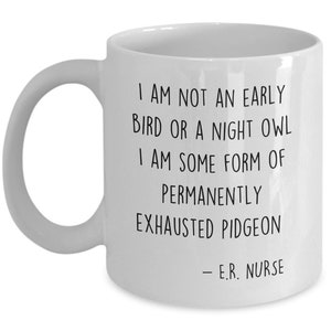 May include: White ceramic coffee mug with black text that reads: "I am not an early bird or a night owl. I am some form of permanently exhausted pigeon - E.R. Nurse."