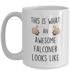 May include: White ceramic coffee mug with a black graphic that says "This is what an awesome falconer looks like" with two thumbs up emojis on either side of the text.