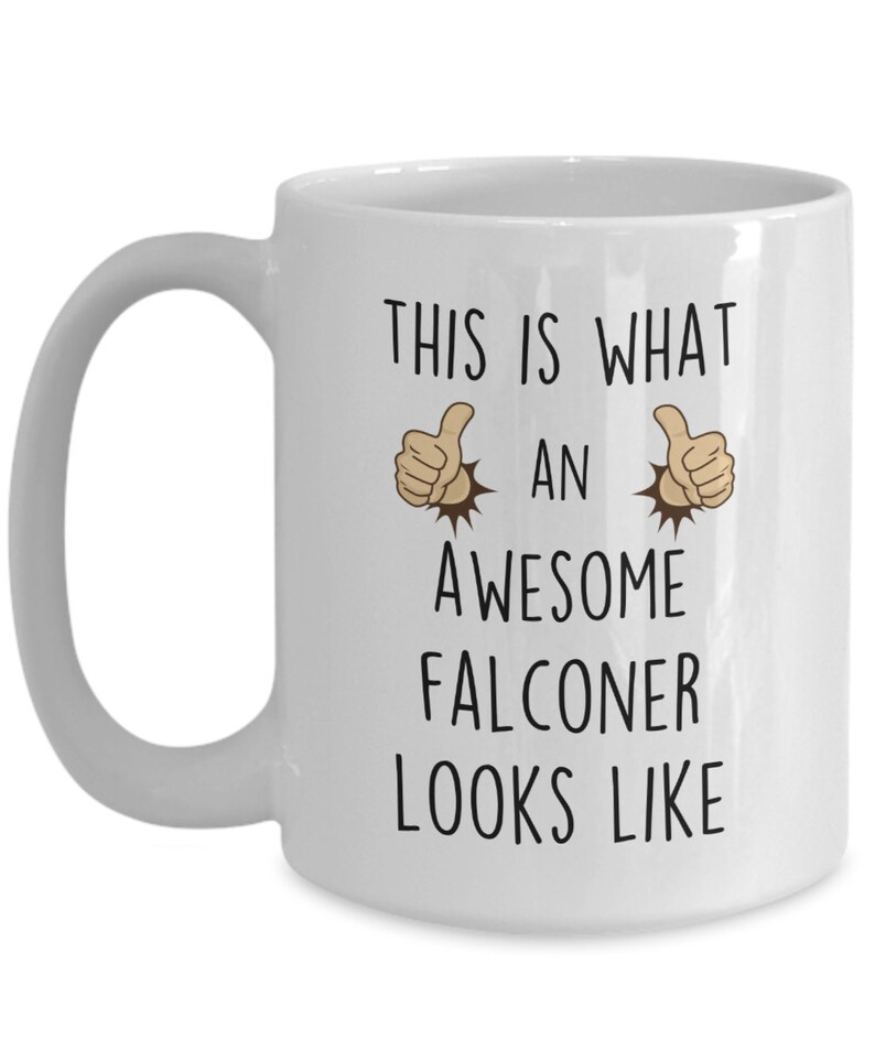 May include: White ceramic coffee mug with a black graphic that says "This is what an awesome falconer looks like" with two thumbs up emojis on either side of the text.