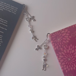 Pu&ograve; includere: Due catene di segnalibro argentate con ciondoli. I ciondoli includono cuori, stelle, note musicali e fiocchi. Le catene sono appese a un libro con un motivo floreale rosa.