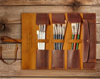 Könnte beinhalten: Eine braune Leder-Künstlerpinselrolle, geöffnet, um verschiedene Pinsel zu zeigen. Die Rolle hat mehrere Taschen und einen Klappenverschluss. Der Text "Have no fear of perfection, you'll never reach it." - Salvador Dali ist sichtbar.