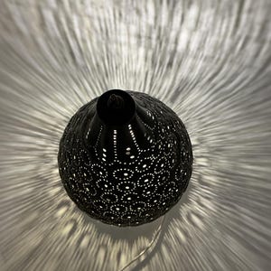 May include: A black, spherical pendant lamp with intricate cut-out patterns. The lamp casts a radial light pattern on the wall. The lamp has a small, cylindrical top and a thin, silver cord.