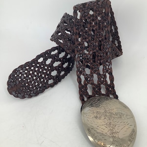 Peut inclure: Une ceinture en cuir marron avec un motif tissé et une boucle argentée ornée d'un motif floral.