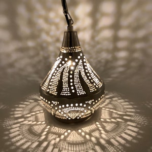 May include: A hanging metal pendant lamp with a teardrop shape. The lamp is dark gray with intricate dot patterns that cast decorative light patterns on the surrounding surface. The lamp is suspended by a chain.