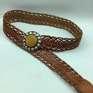 Peut inclure: Une ceinture en cuir tressé marron avec une boucle ronde argentée ornée d'un centre jaune texturé.