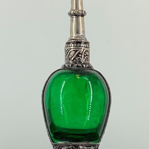 May include: A silver and green glass perfume bottle with intricate detailing. The bottle has a round body and a tall, slender neck with a silver cap.