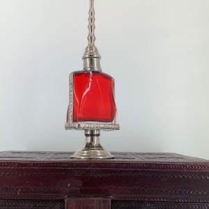 May include: A silver and red glass bottle with a decorative top, sitting on a dark brown wooden box with intricate carvings.