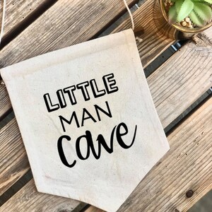 May include: A white canvas banner with black text that reads "LITTLE MAN cave" in a stylized font.