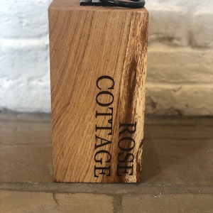 K&ouml;nnte beinhalten: Ein Holz-T&uuml;rstopper mit einem Metallring oben. Der T&uuml;rstopper ist mit den Worten "ROSE COTTAGE" graviert.