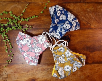 May include: Three fabric face masks with floral patterns. The masks are in shades of pink, blue, and yellow with white flowers.
