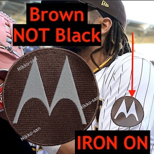 May include: Brown iron-on patch with a white stylized "M" logo. The text "IRON ON" is printed in red below the patch.