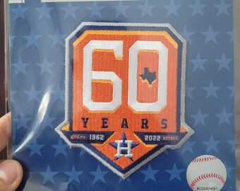 May include: A Major League Baseball collector's patch celebrating the Houston Astros' 60th anniversary. The patch features a large orange number 60 with a white outline, a small Texas star, and the team's logo. The text "YEARS" is below the number, and the years "1962" and "2022" are on either side of the logo.
