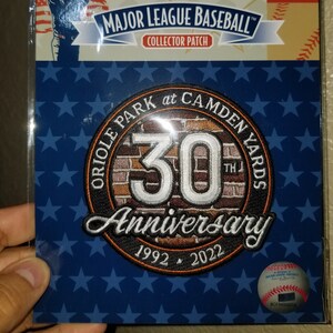 May include: A Major League Baseball collector patch commemorating the 30th anniversary of Oriole Park at Camden Yards, 1992-2022. The patch features a blue background with stars, the MLB logo, and a baseball player silhouette.