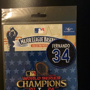 May include: A Major League Baseball collector patch set featuring a blue and white patch with the name "FERNANDO" and the number "34". The set also includes a patch that says "WORLD SERIES CHAMPIONS 2024" with the LA logo, all on a blue background with stars.