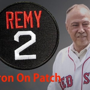 May include: Black and white iron-on patch with the text "REMY" in red and the number "2" in white. The text "Iron On Patch" is below the patch.