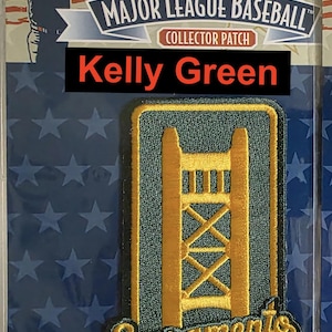 May include: A green and gold embroidered patch featuring the Golden Gate Bridge and the text "Sacramento". The patch is a Major League Baseball collector's patch for Kelly Green.