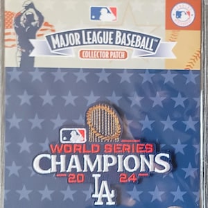 May include: A blue and white World Series Champions patch with a gold trophy and the Los Angeles Dodgers logo. The patch is on a blue background with white stars. The text on the patch reads "World Series Champions 2020 LA 2024".
