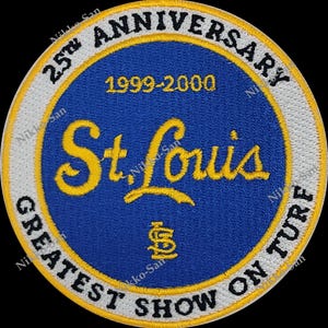 May include: A white and yellow circular patch with the text "25th Anniversary 1999-2000" and "St. Louis Greatest Show On Turf" in a yellow script font. The center of the patch is blue with a white "St. Louis Cardinals" logo.