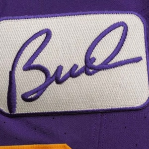 May include: A white patch with a purple embroidered signature that reads "Bud" on a purple background.