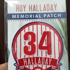 May include: A red, white, and blue embroidered patch with the number 34 in red, the words "Roy Halladay Memorial Patch" and "Halladay" in white, and a red "P" with a white outline.
