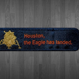 May include: A blue fabric patch with a gold embroidered image of the lunar module and the text "Houston, the Eagle has landed."