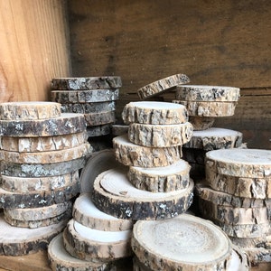 May include: A pile of round wood slices with bark, stacked and arranged in a wooden crate. The wood slices are various sizes and have a natural, rustic look.