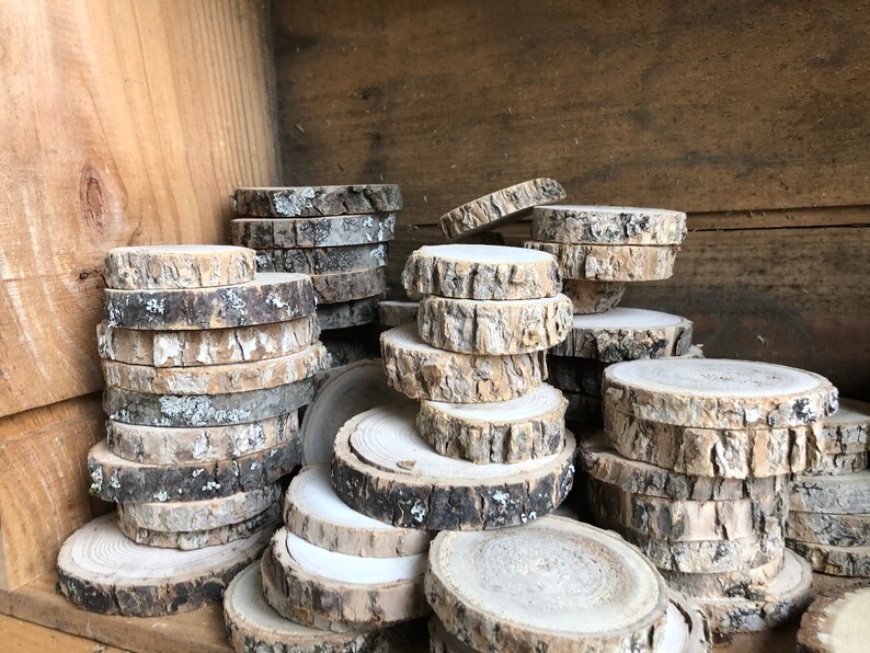 May include: A pile of round wood slices with bark, stacked and arranged in a wooden crate. The wood slices are various sizes and have a natural, rustic look.