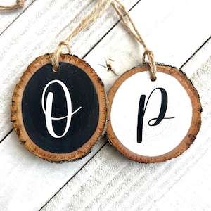 May include: Two wooden ornaments with bark edges. One is painted black with a white "O", the other is white with a black "P". Each has a twine loop for hanging. Rustic, decorative items.