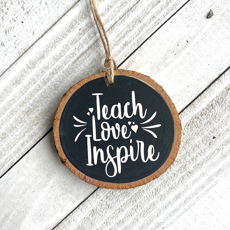 May include: A round wooden ornament with a black background and white text that reads "Teach Love Inspire".