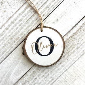 Peut inclure: Une décoration en bois blanc avec une lettre noire "O" et le nom "Oliver" écrit en lettres dorées.
