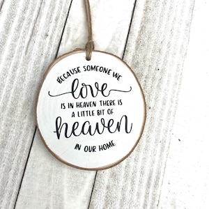 May include: White wooden round ornament with black text that reads "Because someone we love is in heaven there is a little bit of heaven in our home".