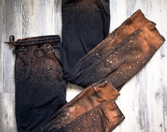 May include: Two pairs of black sweatpants with a bleach splatter design. The sweatpants have a drawstring waistband and a relaxed fit.