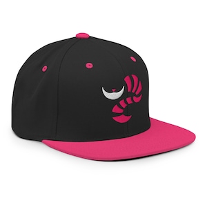 Könnte beinhalten: Eine schwarze und rosafarbene Baseballkappe mit einem rosafarbenen gestickten Cheshire-Katzen-Design. Das Grinsen der Katze ist weiß.