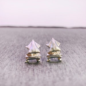 May include: A pair of silver earrings shaped like a sailboat. The earrings are small and delicate, and they have a modern and minimalist design.