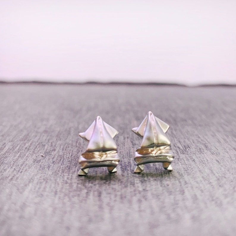 May include: A pair of silver earrings shaped like a sailboat. The earrings are small and delicate, and they have a modern and minimalist design.