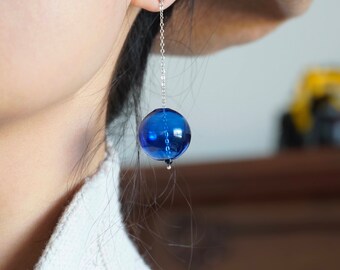 May include: A pair of long, silver chain earrings with a large, round, blue glass bead at the end of each chain.